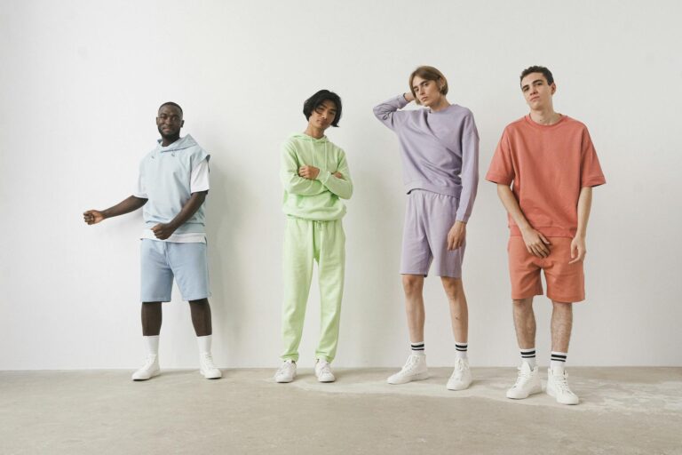 Four men pose in trendy pastel casual wear against a white background.