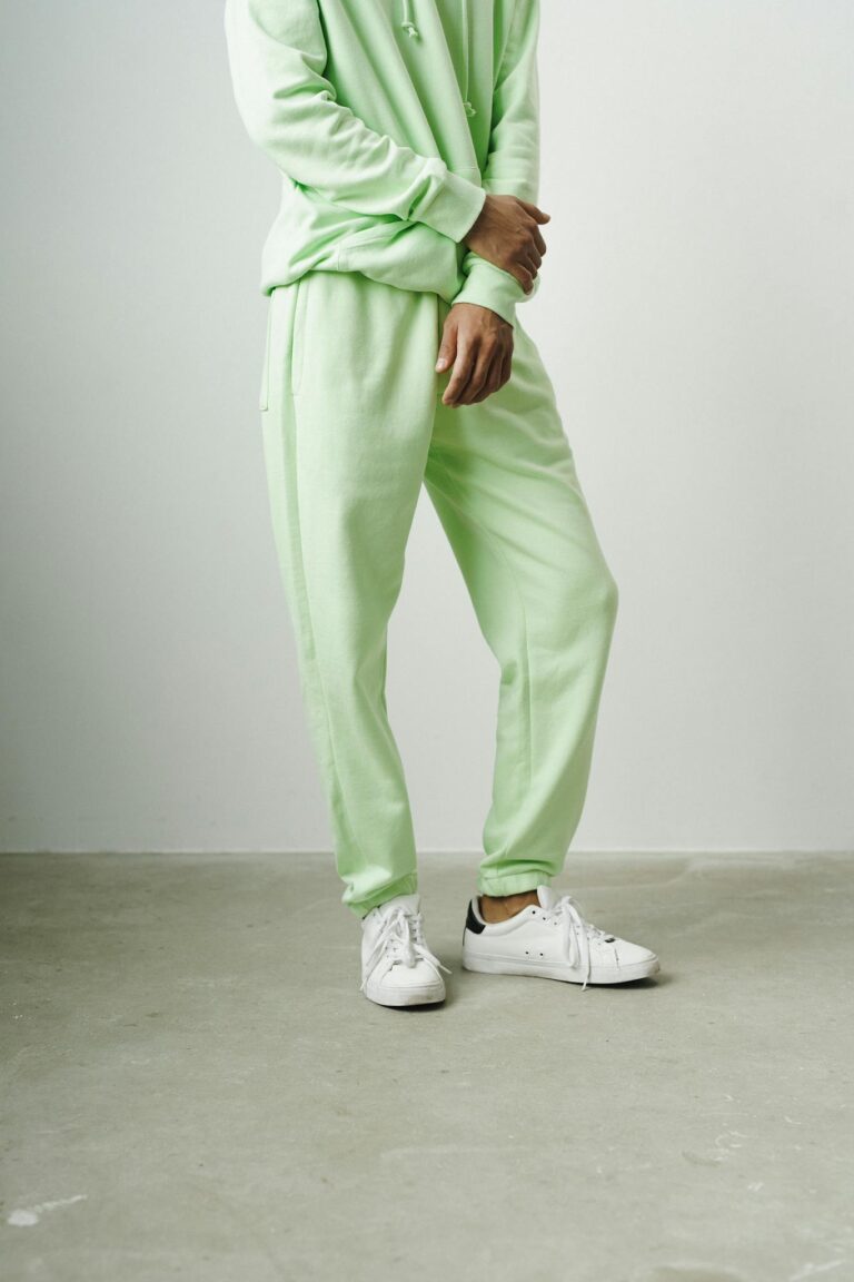 Man in a green tracksuit and white sneakers, minimalist studio setting.